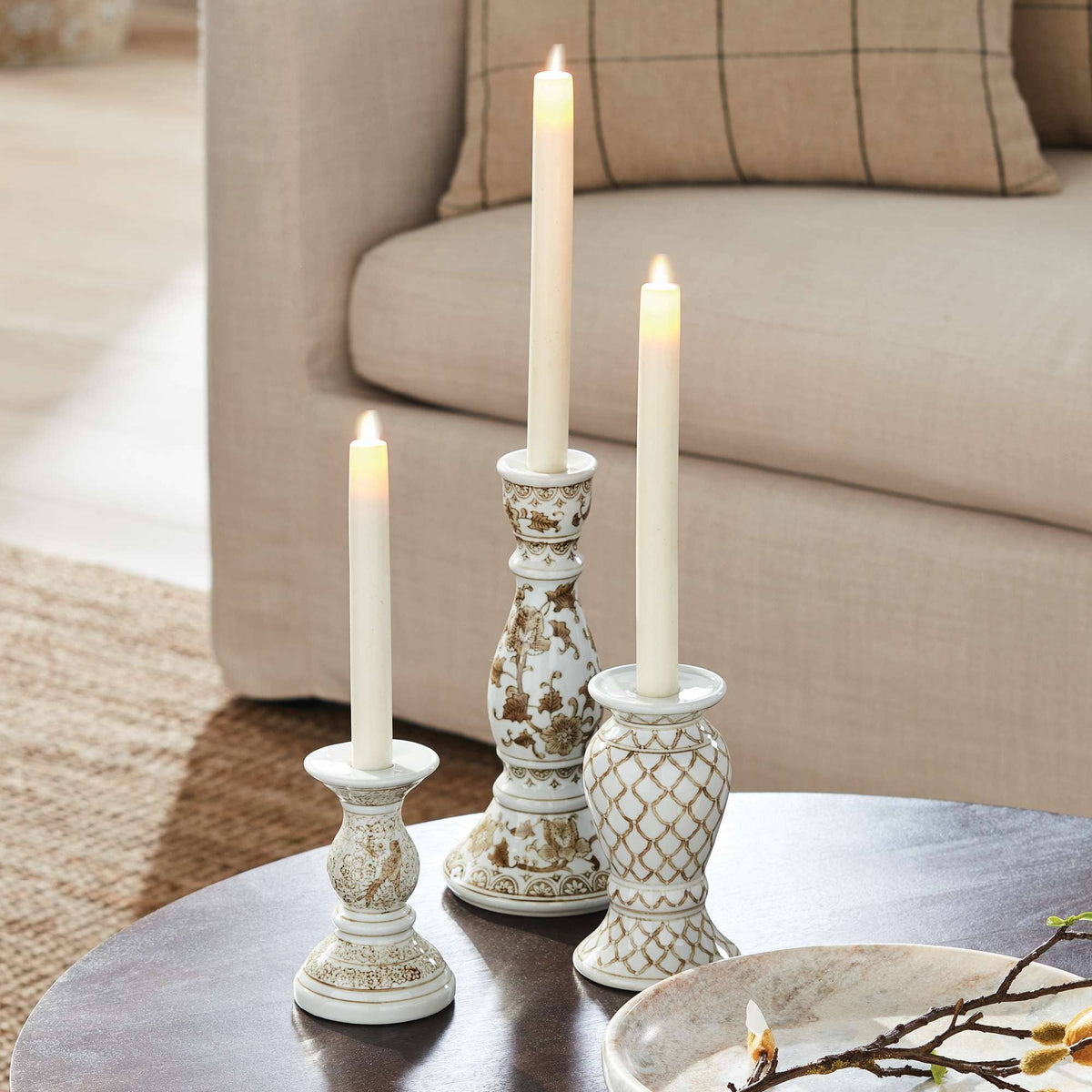 Decorative candles in ornate holders on a coffee table with a couch in the background