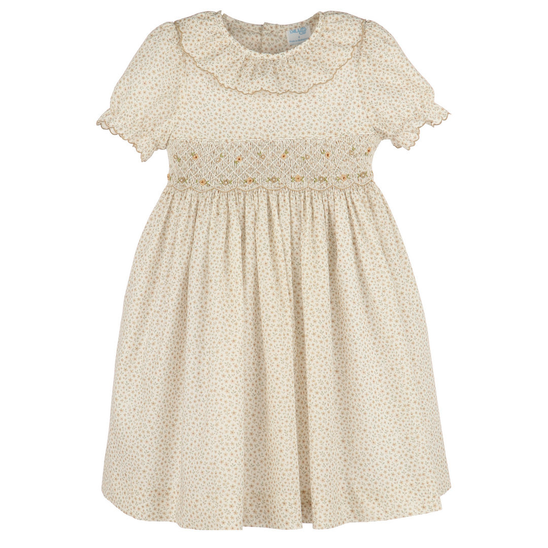 A cream-colored babydoll dress with a tiny gold dot pattern, featuring a ruffled collar, short flutter sleeves, and smocked detailing across the chest.