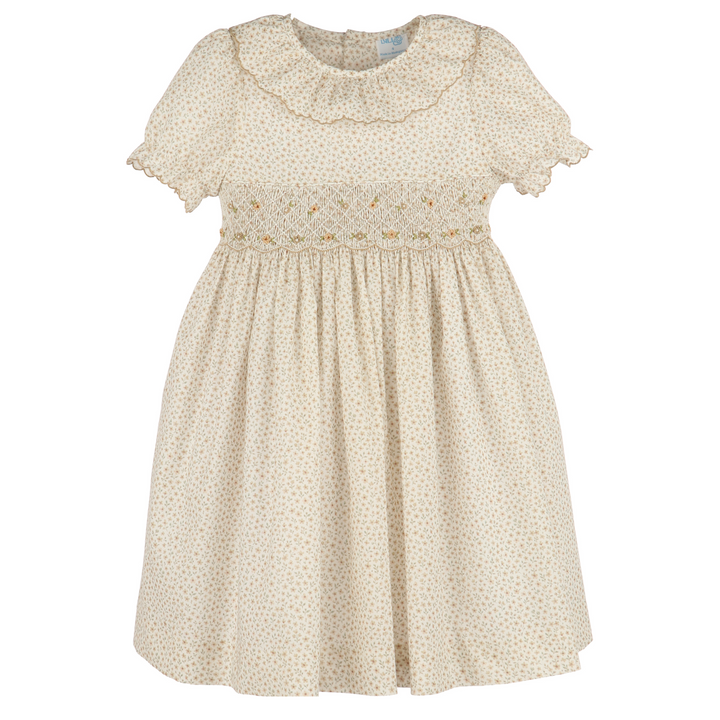 A cream-colored babydoll dress with a tiny gold dot pattern, featuring a ruffled collar, short flutter sleeves, and smocked detailing across the chest.