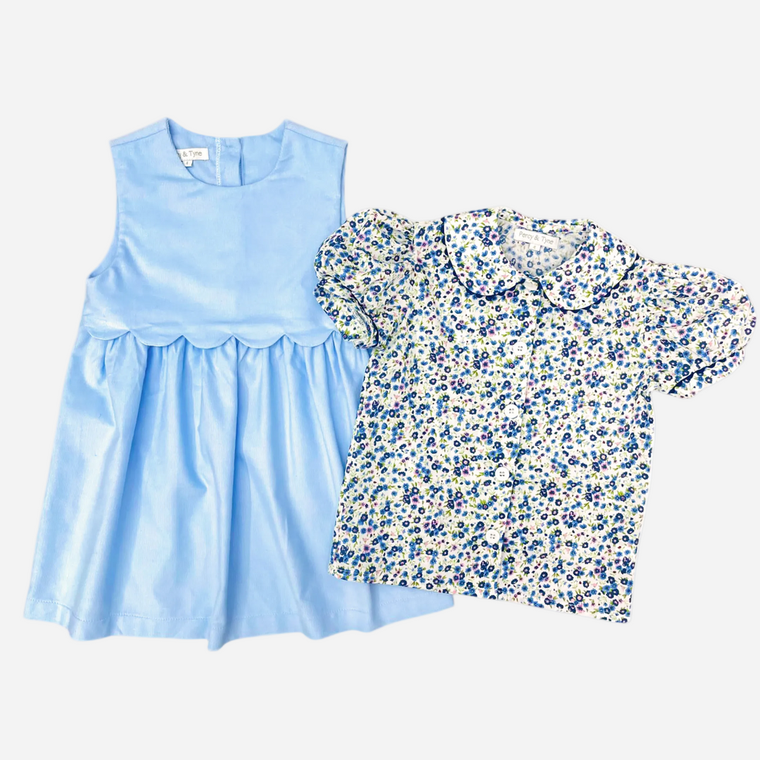 A two-piece girls' outfit set on a white background, featuring a light blue sleeveless dress with a ruffled hem and a short-sleeve button-up blouse with a blue, green, and white floral print.