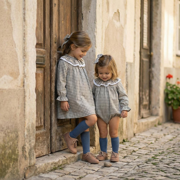two girls wearing plaid outfits in front of rustic door on cobblestone street