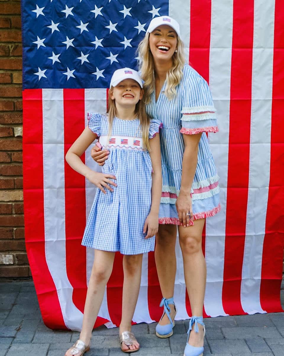 Two people in matching outfits standing in front of an American flag.