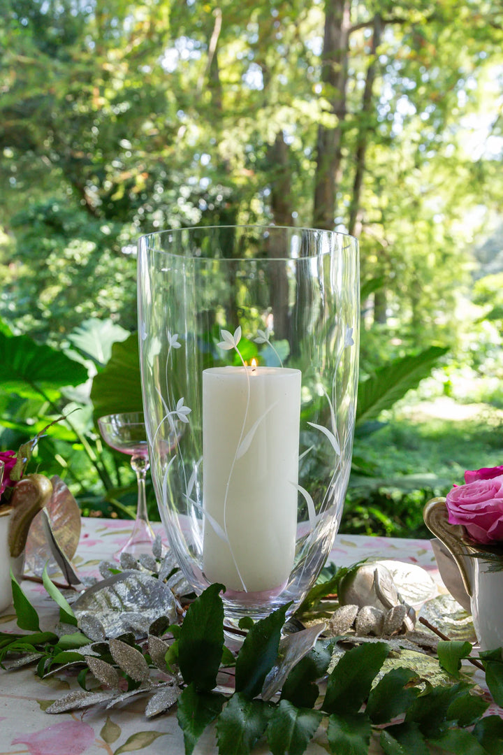 Candle in a glass holder on a table with floral decorations outdoors.