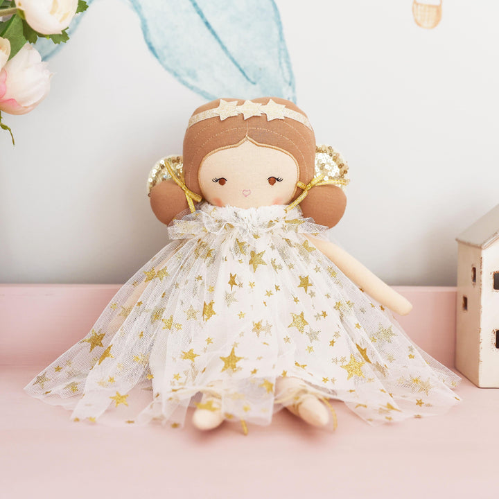 Doll in a star-patterned dress sitting on a pink surface with flowers and small houses in the background.