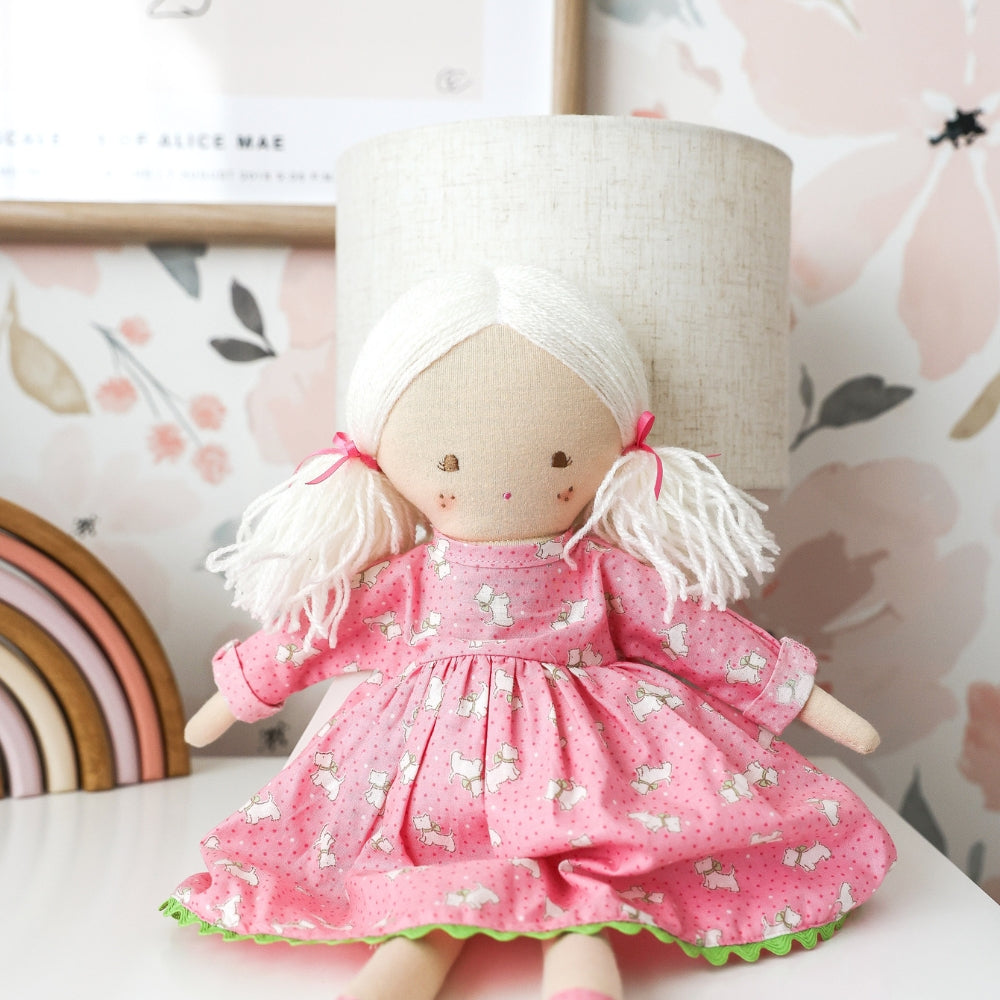 Textile doll in a pink dress with white hair, sitting on a surface with a soft focus background.