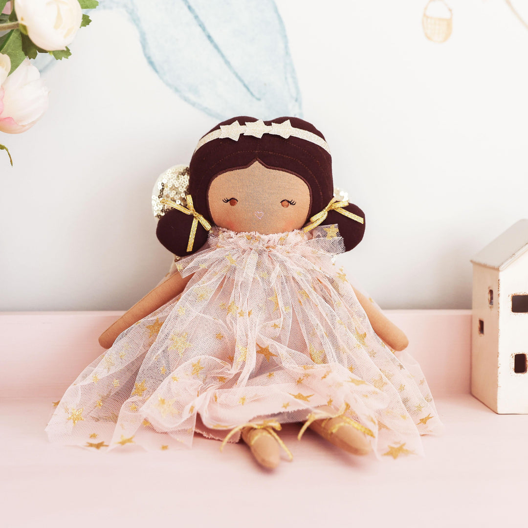 Doll in a light dress with flowers and small houses in the background