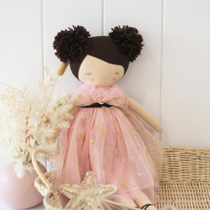 Doll with pink dress and brown hair styled in buns on a white background