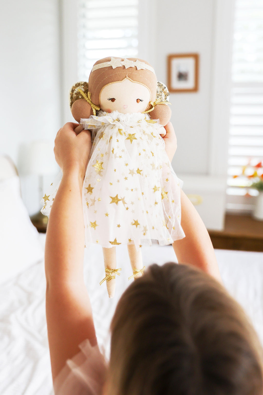 Child holding a doll with a star-patterned dress in a bright room.