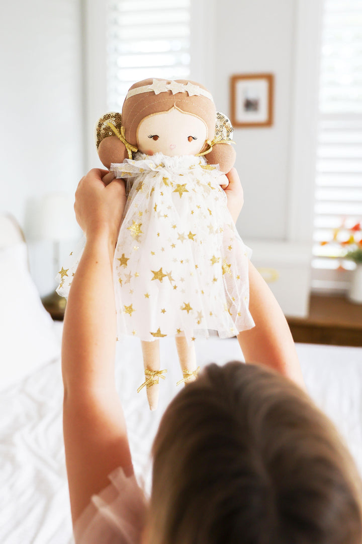 Child holding a doll with a star-patterned dress in a bright room.