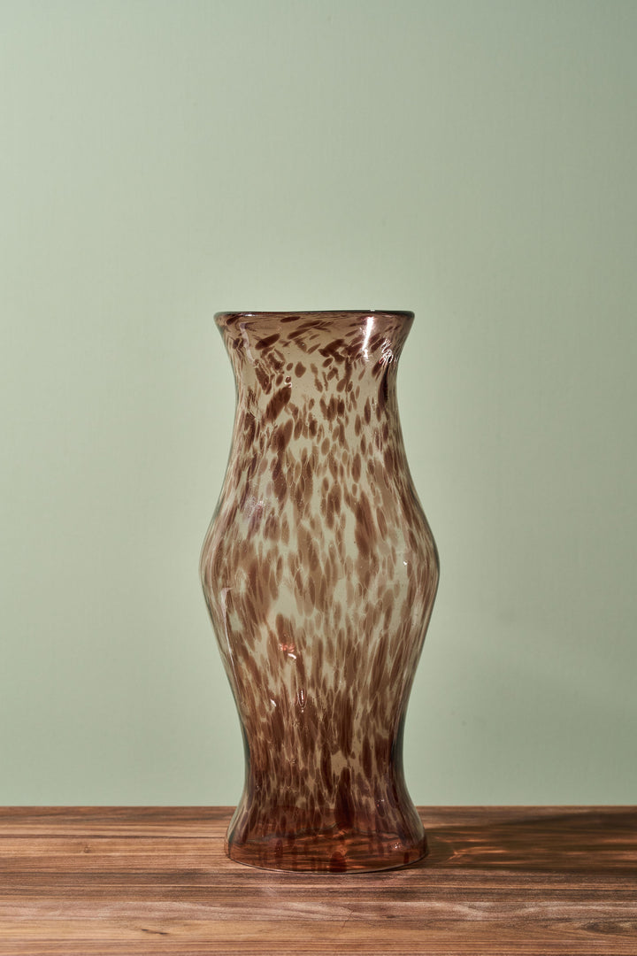 A brown and beige mottled glass vase with a flared rim, standing on a wooden surface against a pale green background.