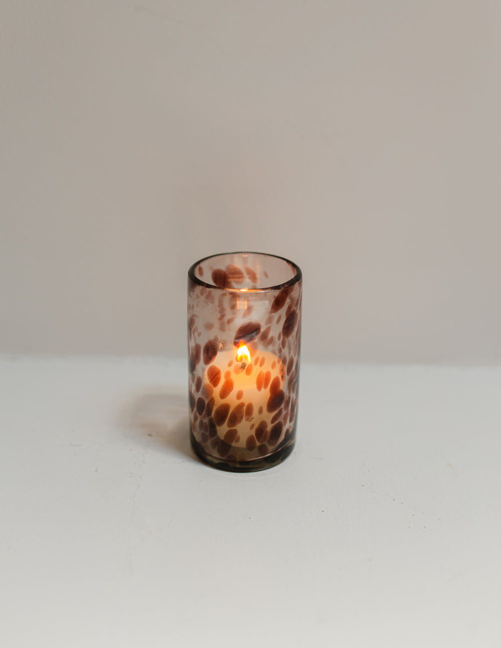 Glass candle holder with a lit candle on a white surface and light gray background