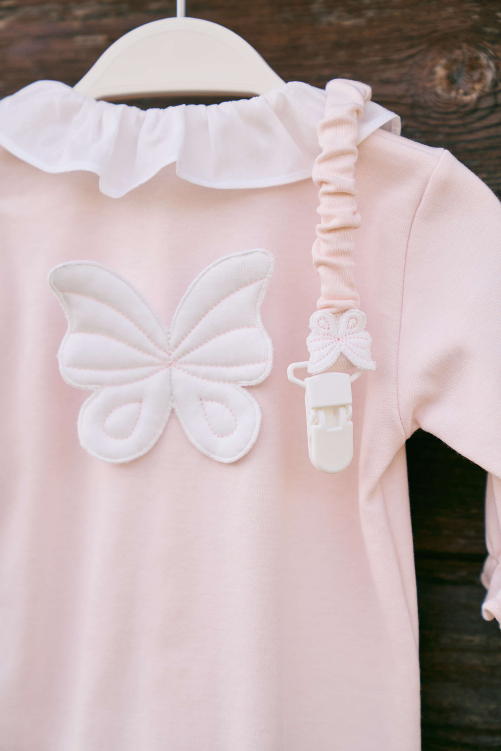 Pink baby dress with white butterfly design on a wooden surface