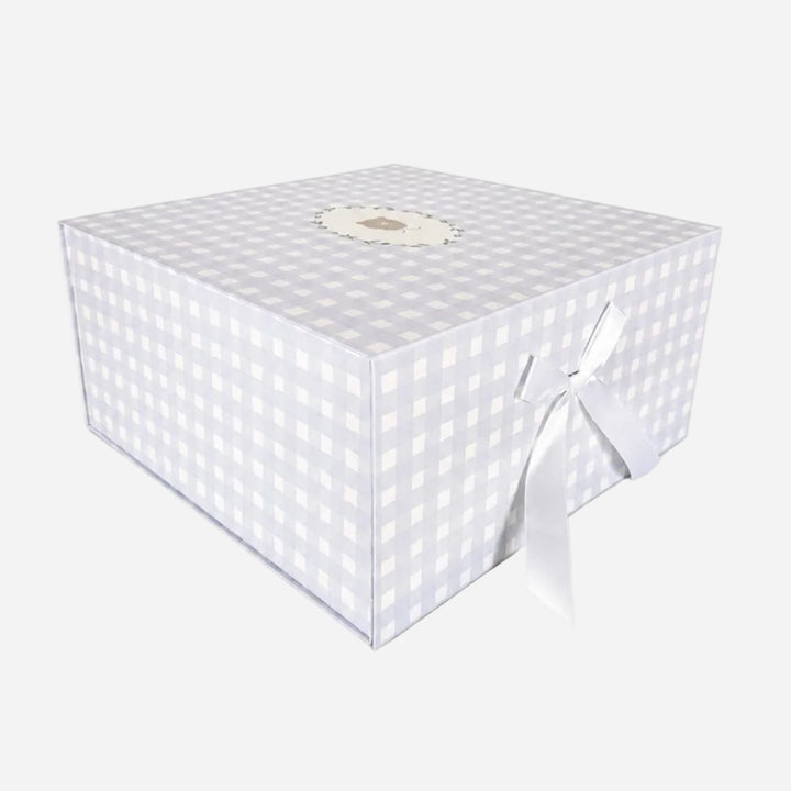 A square gift box with a light gray and white gingham checkered pattern, featuring a white satin ribbon tied in a bow on one side and a small round decorative label on top, set against a plain white background.