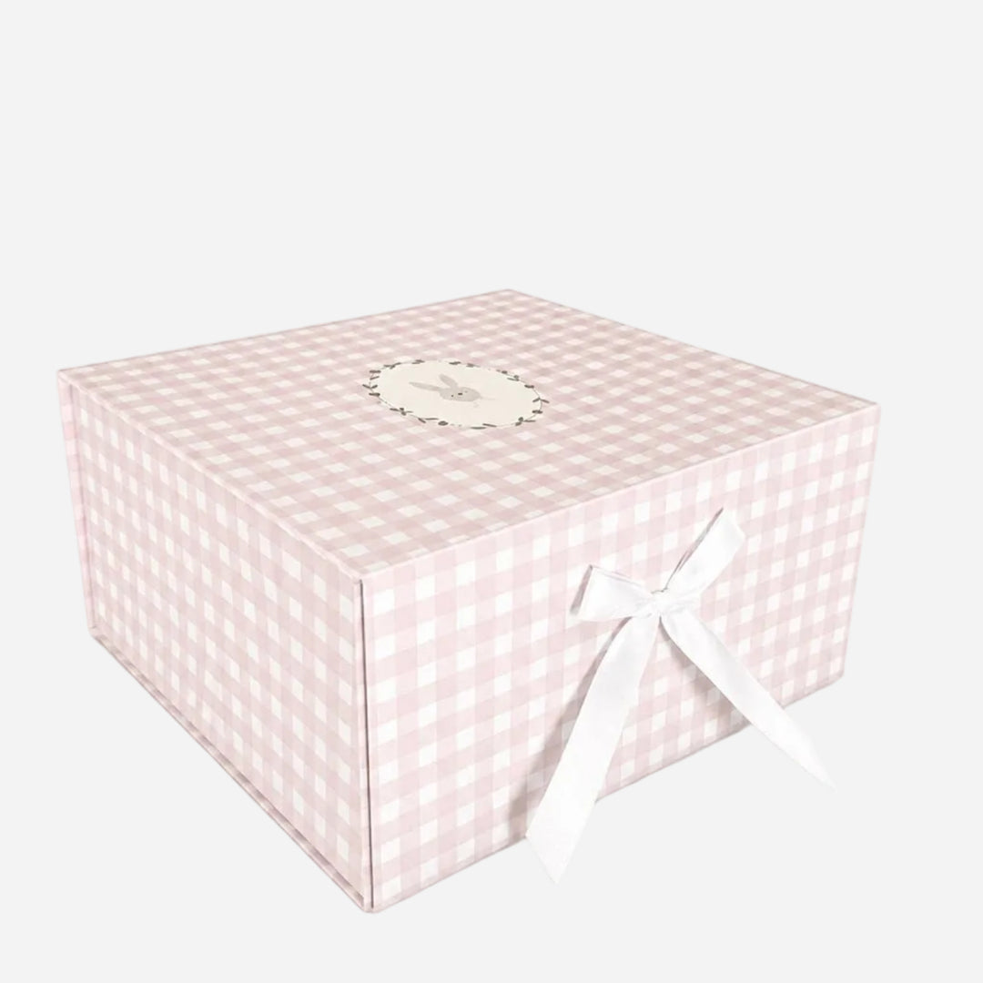 A square gift box with a light pink and white gingham checkered pattern, decorated with a white ribbon bow on the front and a small round label on top, set against a plain white background.