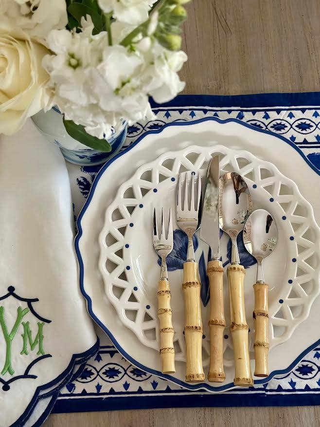 Set of cutlery with bamboo handles on a decorative plate with floral arrangement in the background.