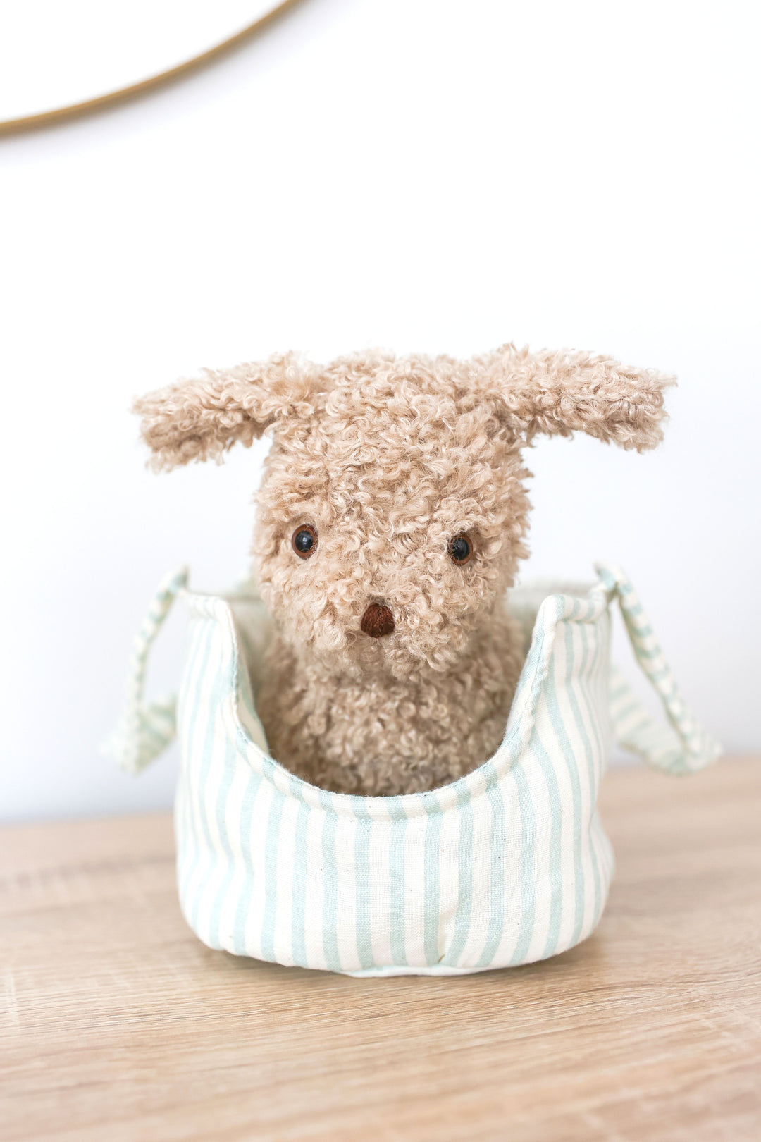 Small plush dog toy in a striped fabric basket on a wooden surface with a white background