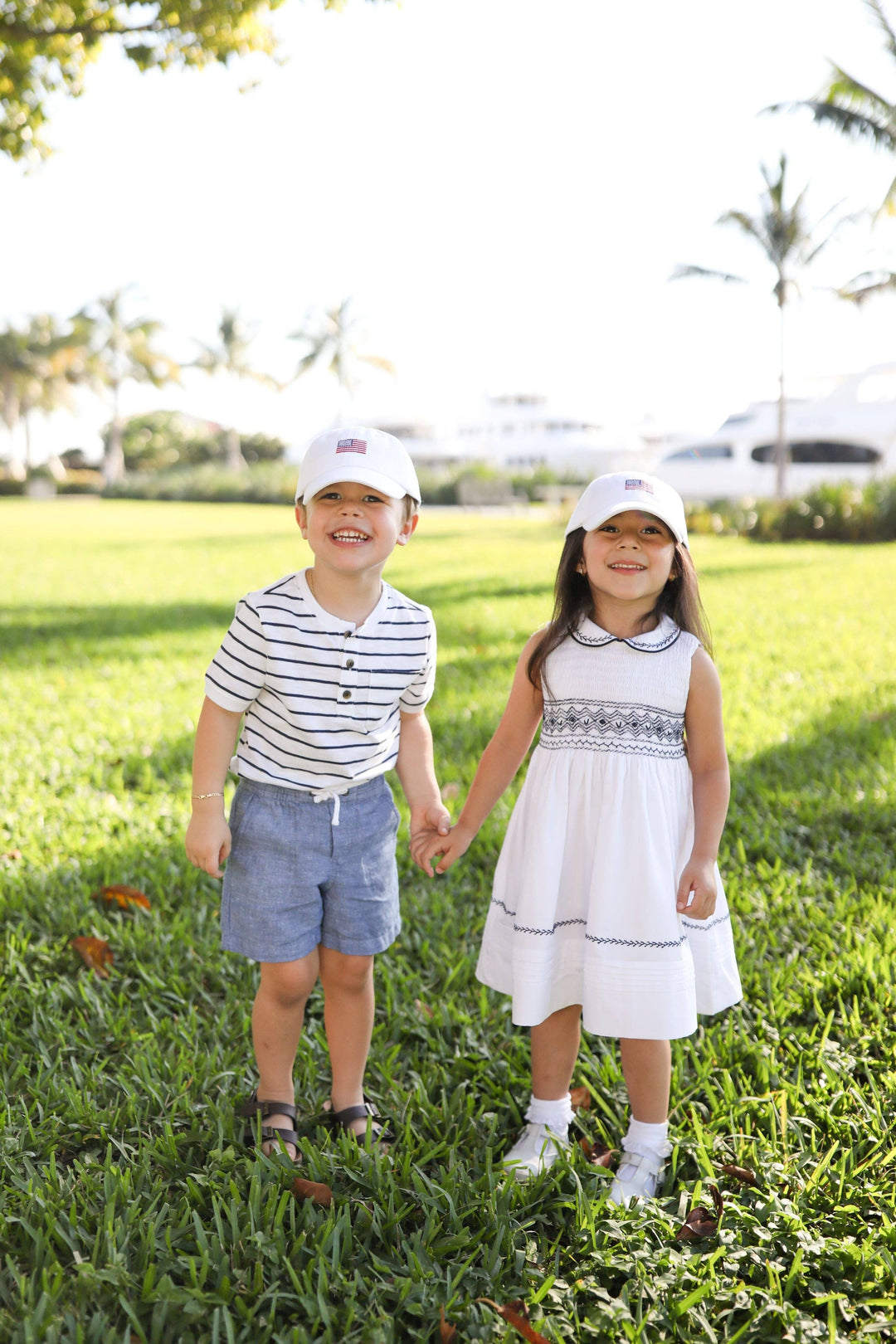 Two children holding hands in a grassy field with trees in the background