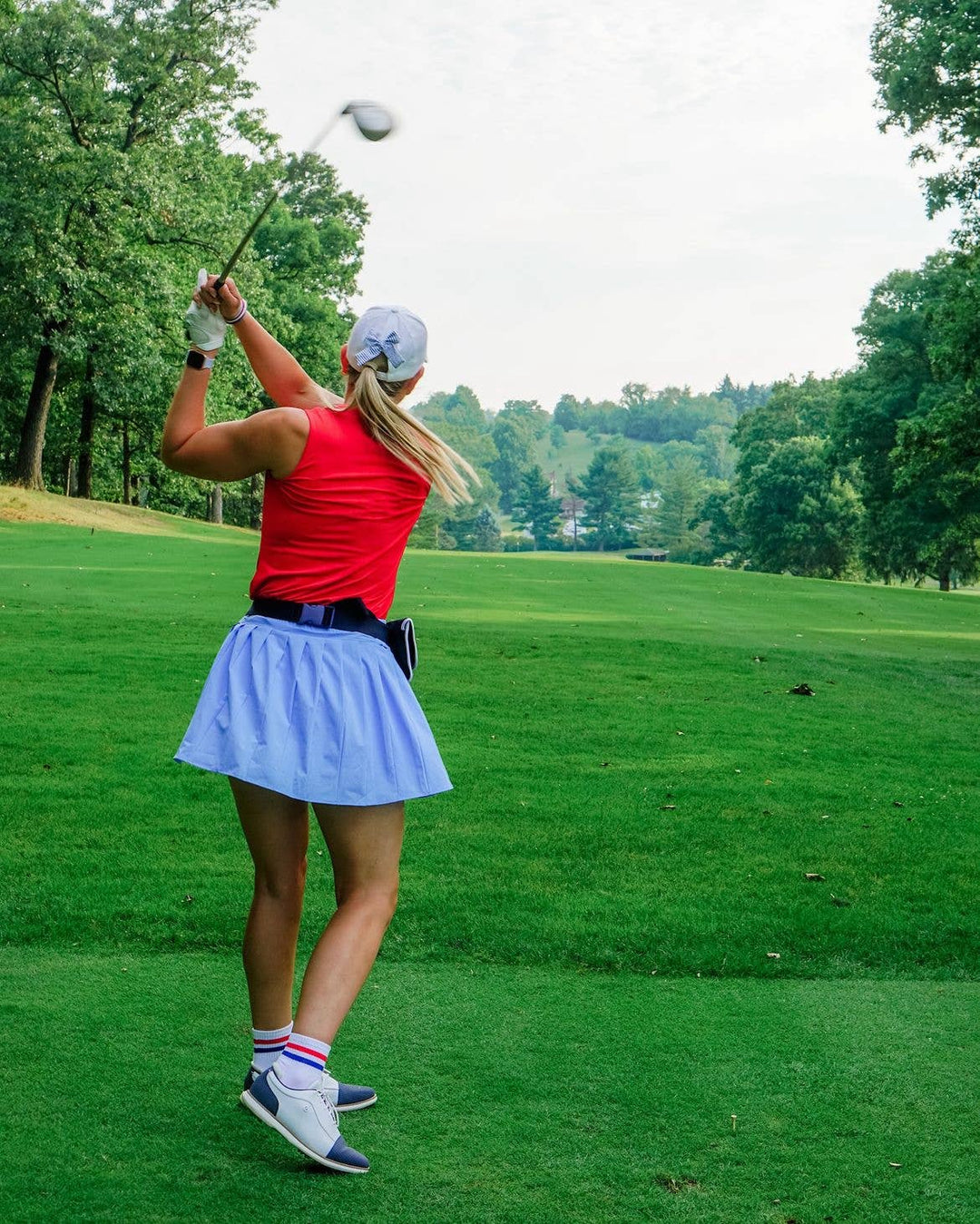 Woman playing golf on a green course with trees in the background