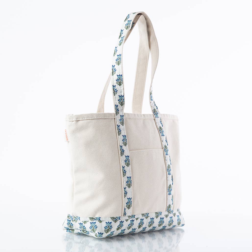 An off-white canvas tote bag with blue and green floral patterned straps and bottom trim, shown on a clean white background.