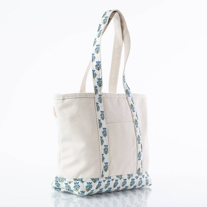 An off-white canvas tote bag with blue and green floral patterned straps and bottom trim, shown on a clean white background.