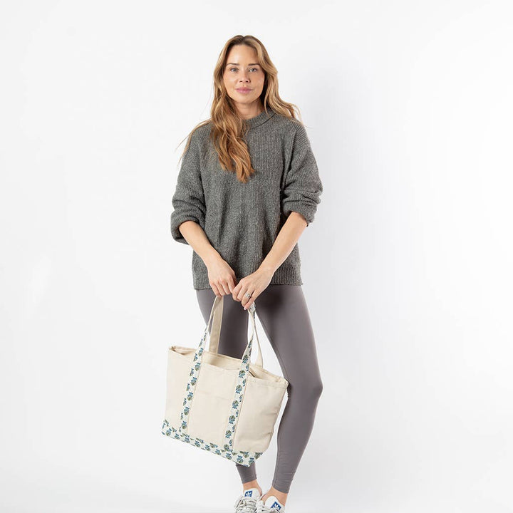 Woman holding a beige tote bag with floral straps on a white background