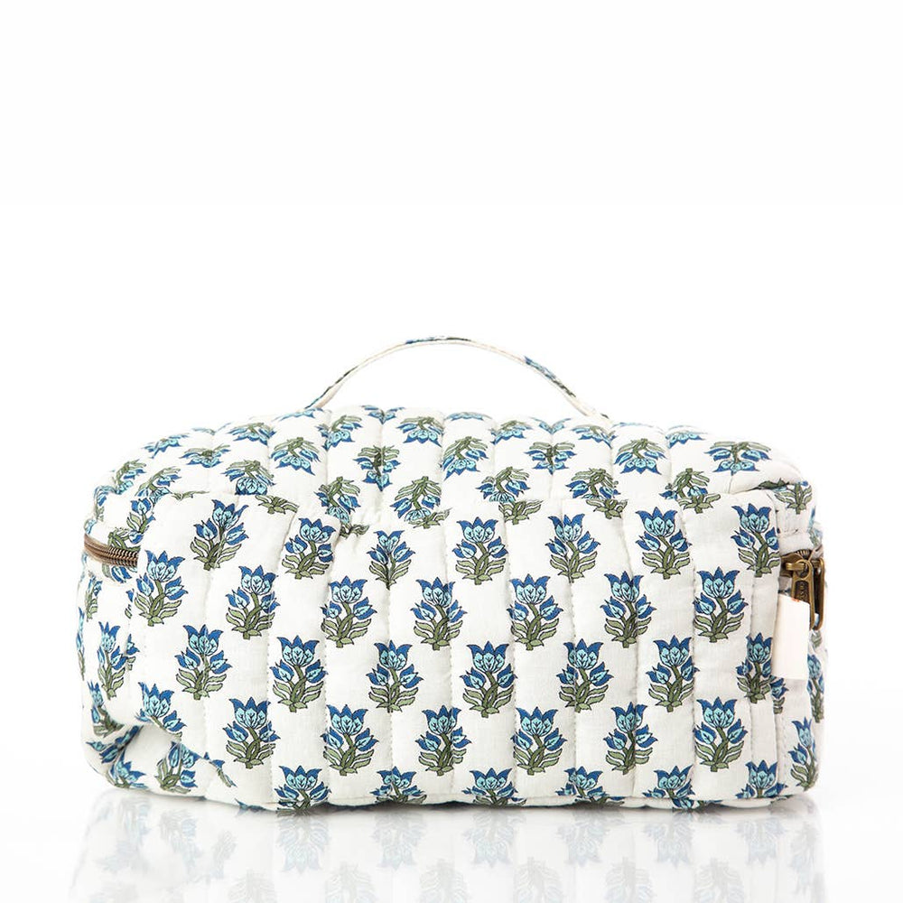 A quilted cosmetic bag with a white background and a repeating blue and green floral block print, featuring a top handle and gold-tone hardware.