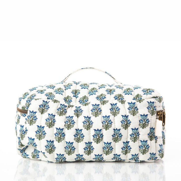 A quilted cosmetic bag with a white background and a repeating blue and green floral block print, featuring a top handle and gold-tone hardware.