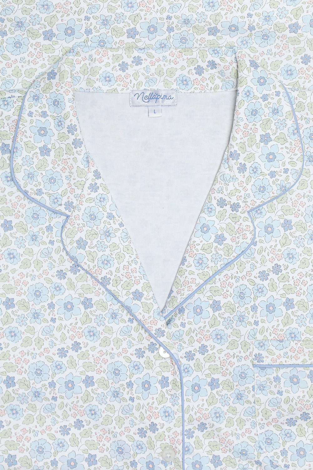 Close-up of a pajama top with a light blue, white, and green floral pattern, featuring light blue piping and a white inner collar.