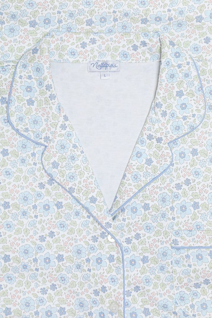 Close-up of a pajama top with a light blue, white, and green floral pattern, featuring light blue piping and a white inner collar.