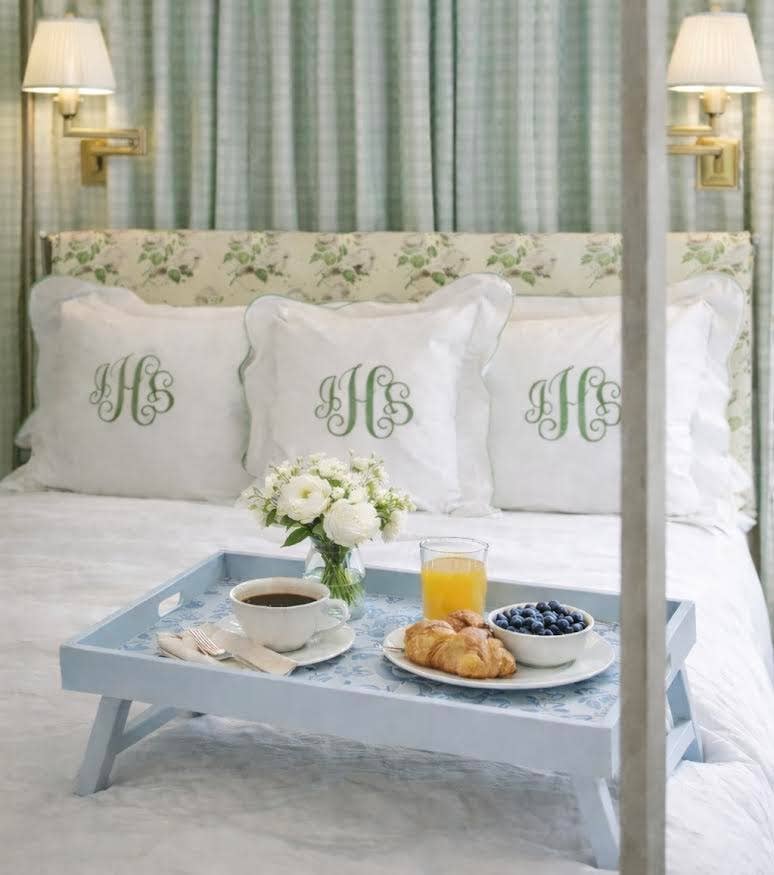 Bedroom with a four-poster bed, monogrammed pillows, and a breakfast tray.