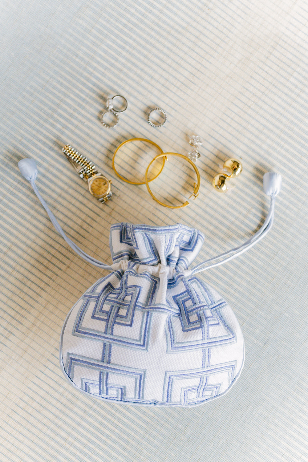 Drawstring bag with geometric pattern, gold rings, and earrings on a textured surface
