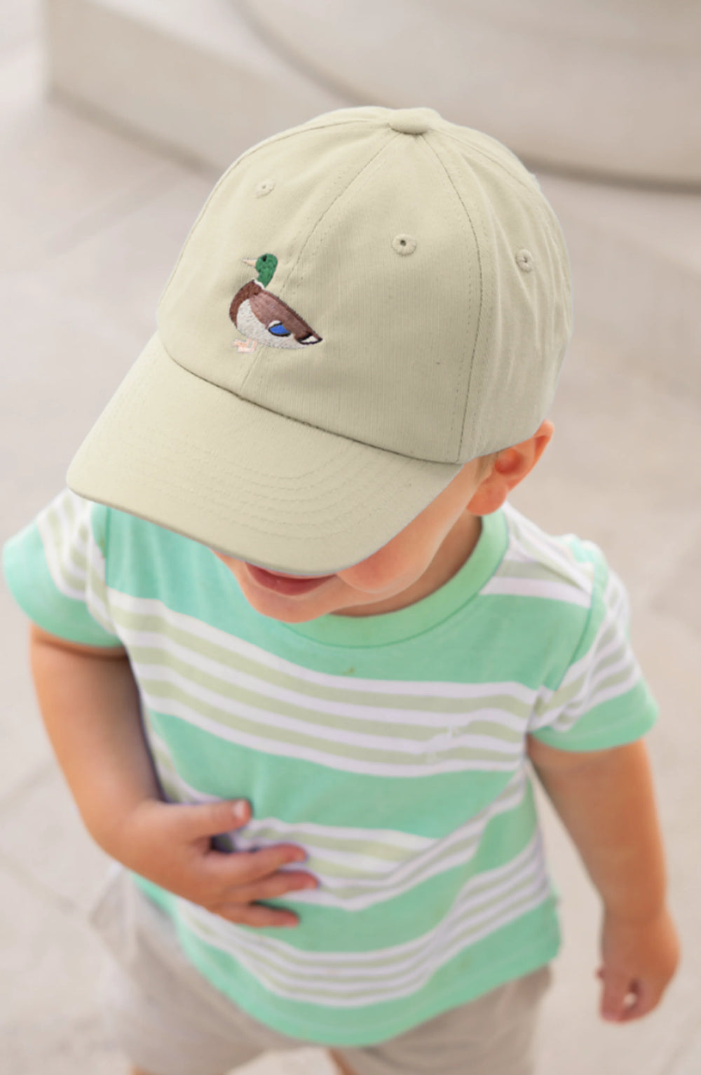 Child wearing a light green cap with an embroidered design and a matching striped shirt.