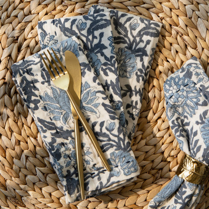 Floral-patterned napkin with gold fork and knife on a woven surface