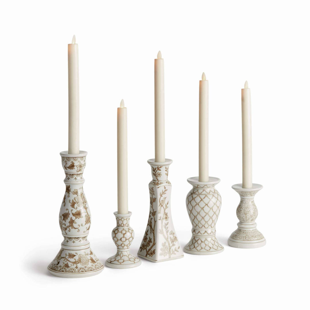 Five ornate cream ceramic candlesticks with gold floral and geometric patterns, each holding a white taper candle, arranged in a row against a white background.