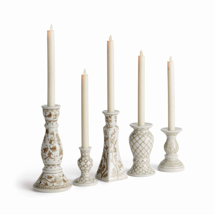 Five ornate cream ceramic candlesticks with gold floral and geometric patterns, each holding a white taper candle, arranged in a row against a white background.