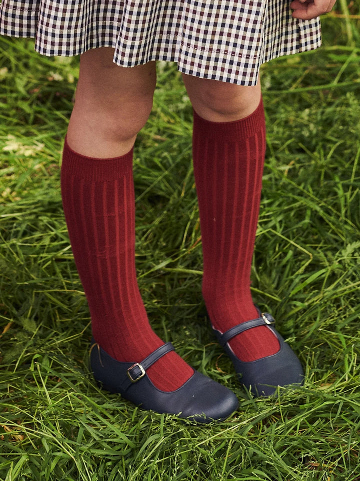 Person wearing red knee-high socks and navy shoes on grass