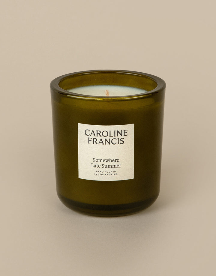 Green candle in a glass jar with 'Caroline Francis' label on a beige background