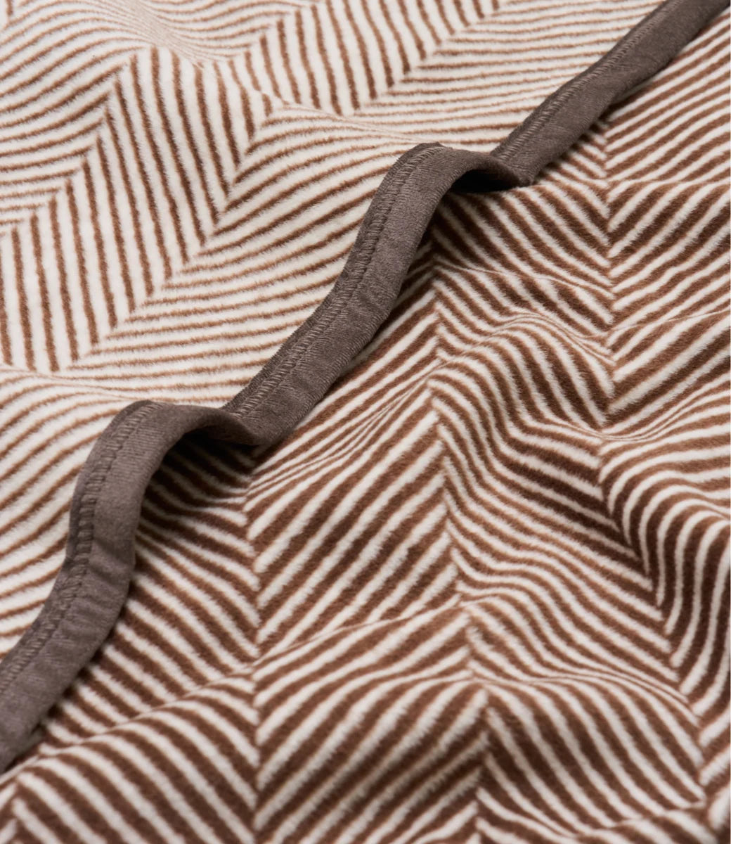 Close-up of a textured fabric with a brown and beige herringbone pattern and a contrasting solid brown trim.