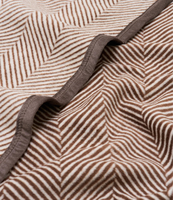 Close-up of a textured fabric with a brown and beige herringbone pattern and a contrasting solid brown trim.