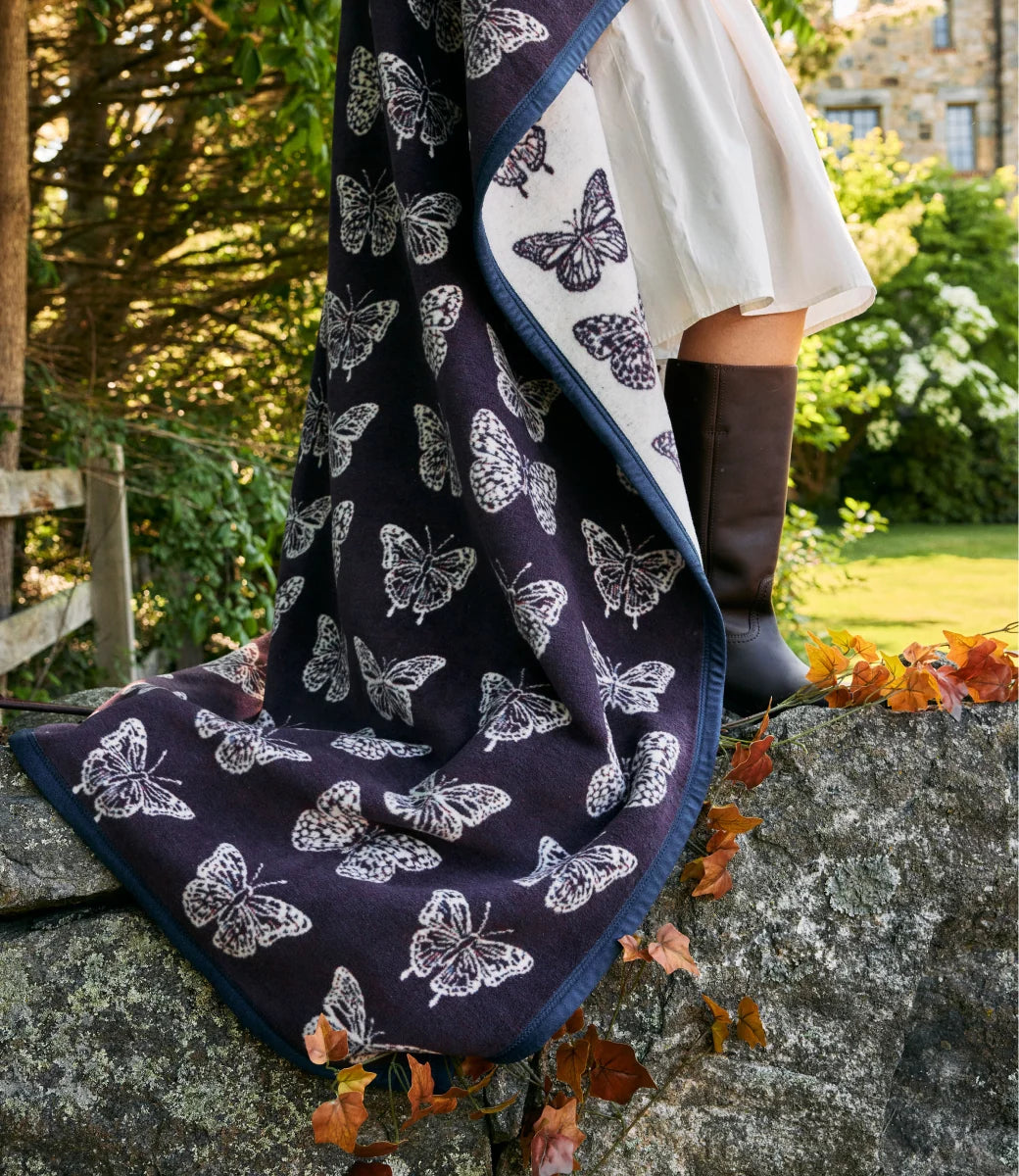 A dark navy blanket with a white butterfly pattern draped over a stone wall outdoors, with part of a person wearing a white dress and black boots visible.