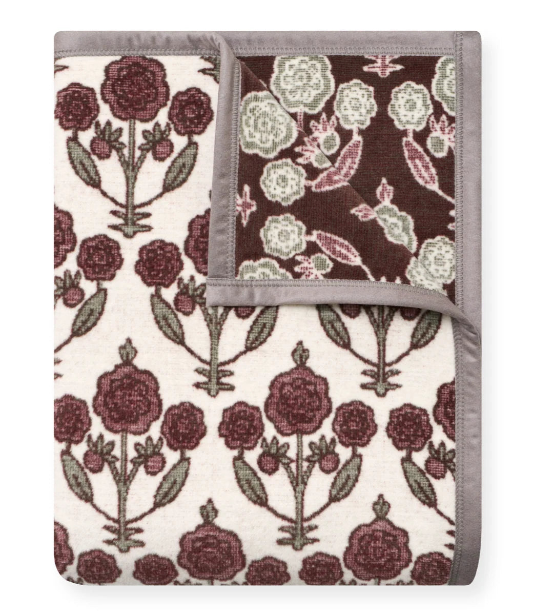A folded patterned blanket or throw with a cream background, dark burgundy floral motifs, muted green leaves, and a gray border, shown on a plain white background.