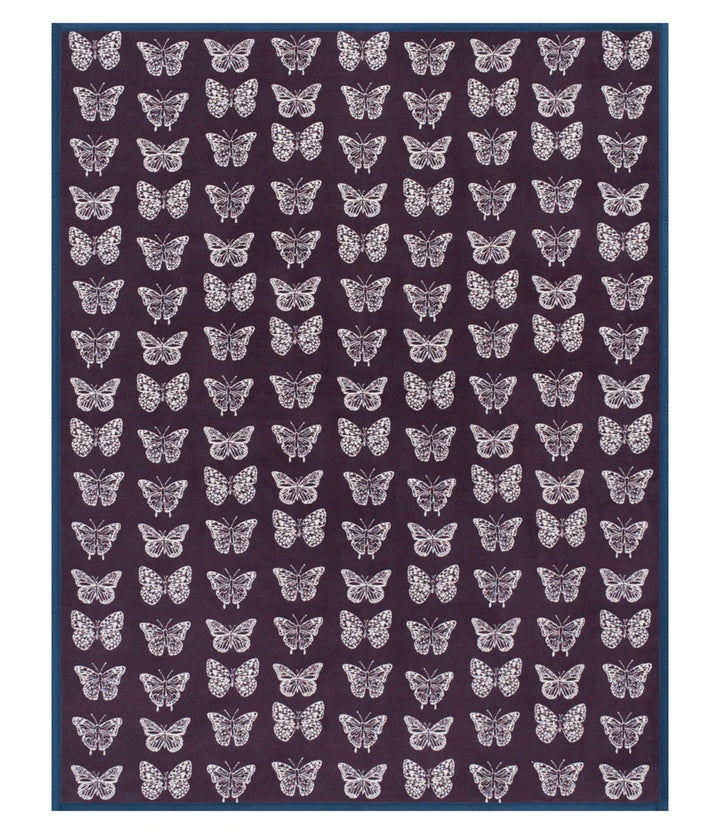 A rectangular rug featuring a repeating pattern of white butterflies on a dark plum-purple background, finished with a solid dark blue border.