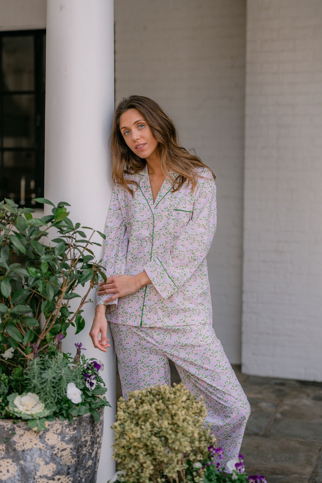 Woman in a floral pajama set standing next to a white column with plants around.