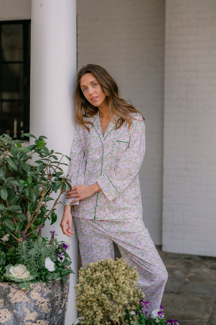 Woman in a floral pajama set standing next to a white column with plants around.