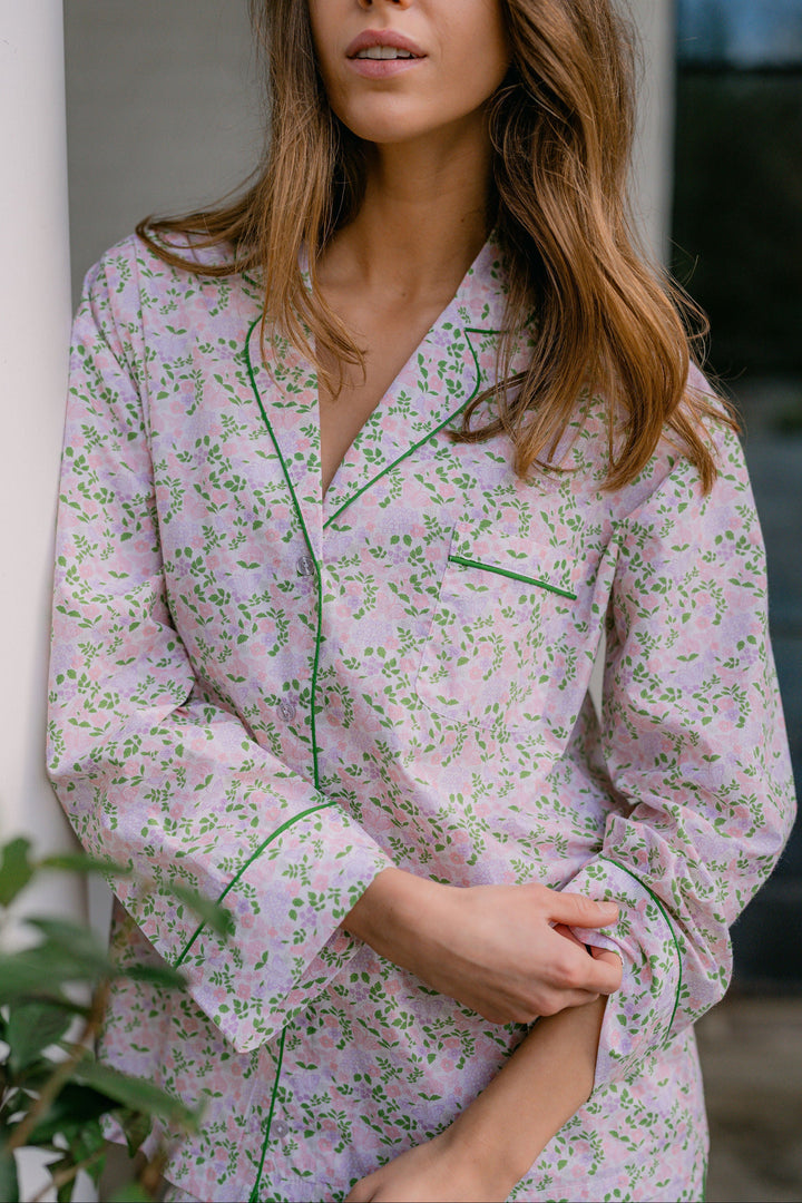 Woman wearing a floral pajama set with green piping, standing outdoors.