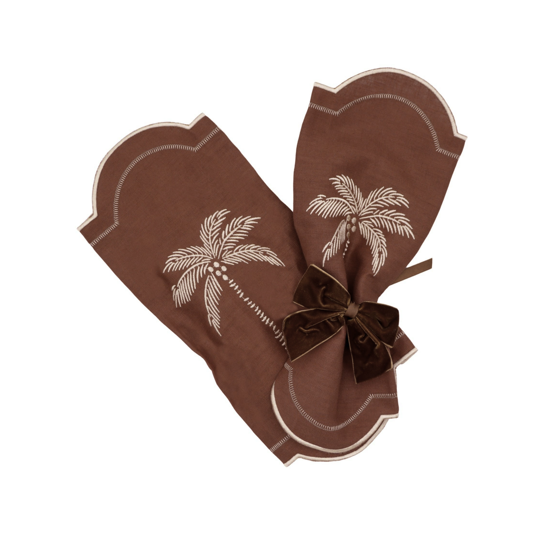 A pair of brown baby mittens with white palm tree embroidery and a matching brown velvet bow, displayed on a clean white background.