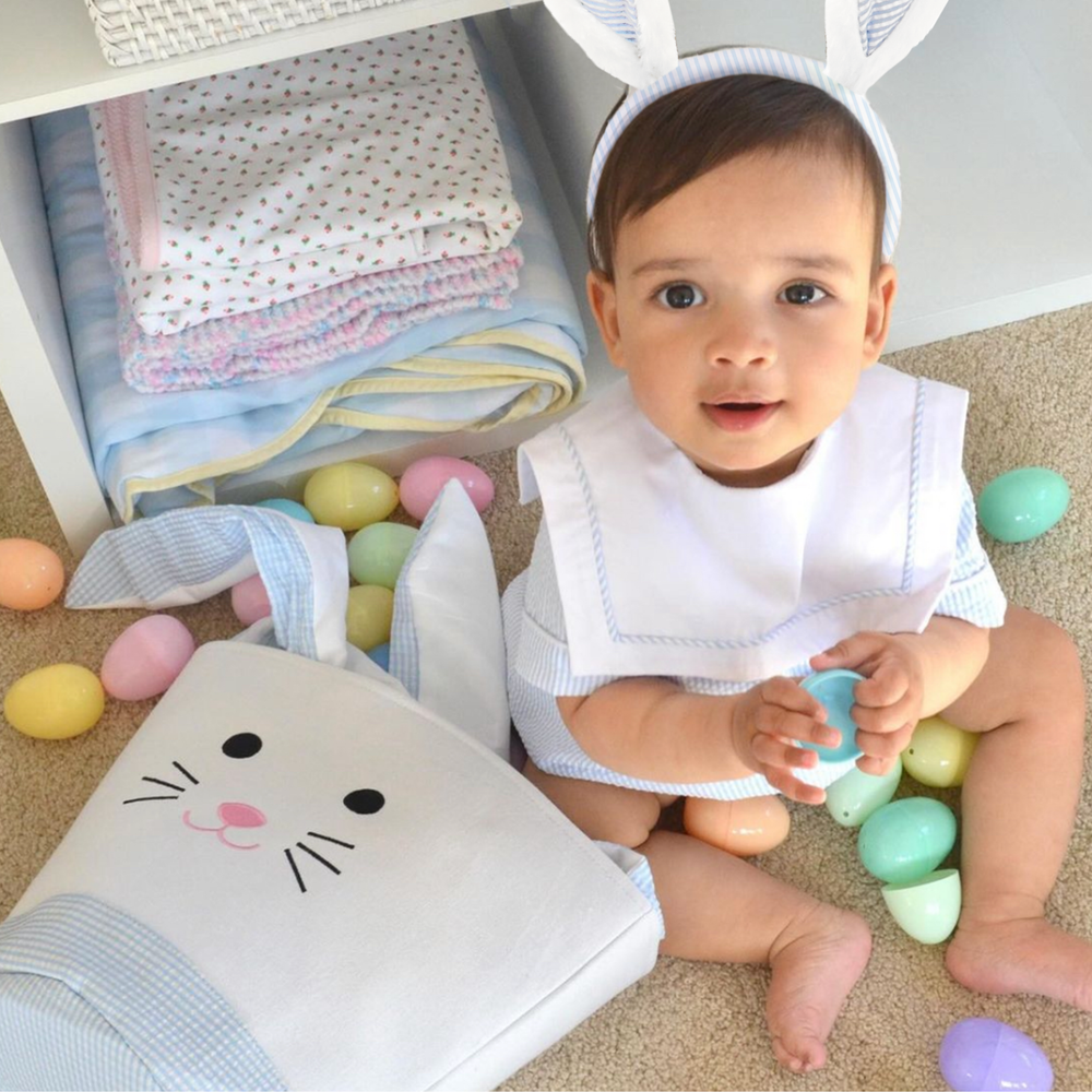 Toddler Boy wearing play bunny ears sitting next to an easter basket with easter eggs