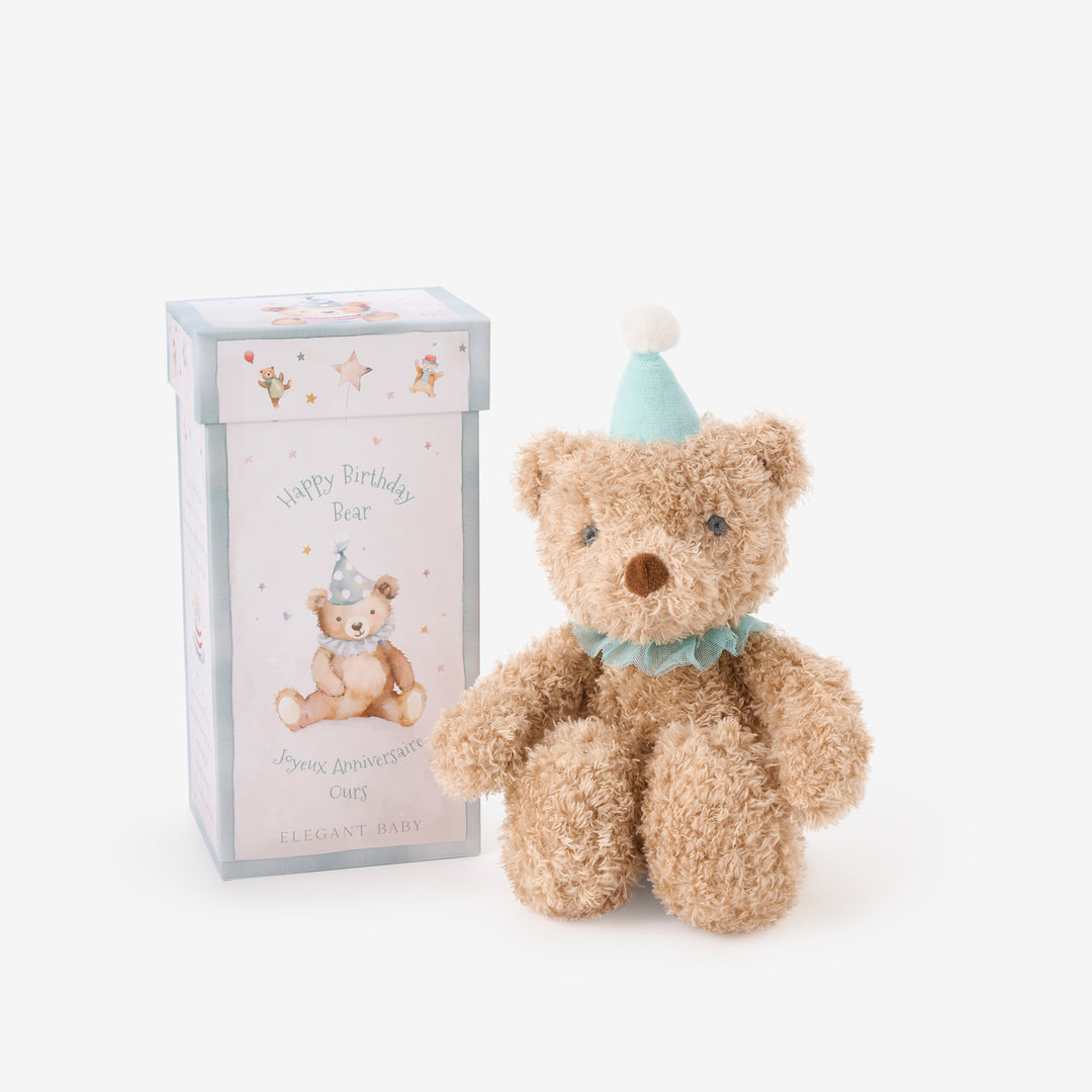 Teddy bear with a birthday hat next to a gift box on a white background
