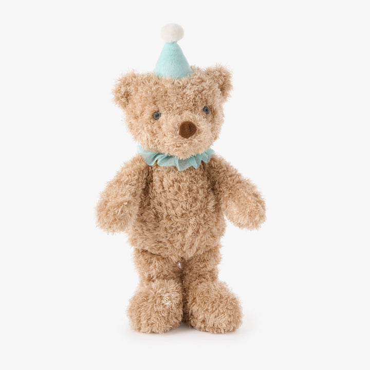 Stuffed teddy bear wearing a party hat and bow tie on a white background