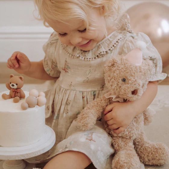 Child holding a teddy bear next to a small cake with a bear figurine
